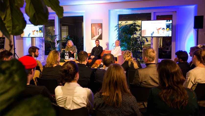 two speakers on stage with presenter in coworking space with large audience attending