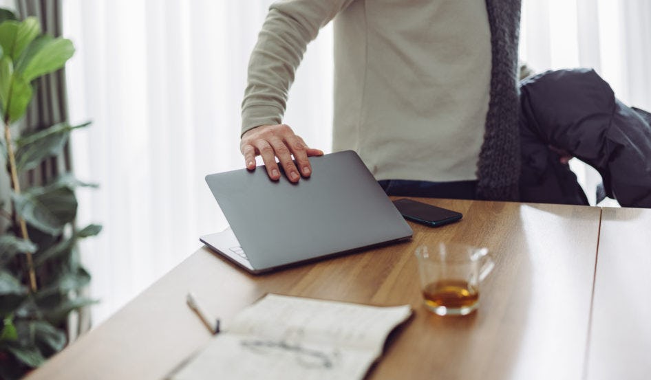 Close up photo of businessman hand closing laptop computer while standing at desk in the living room and with scarf and jacket, ready to go out.